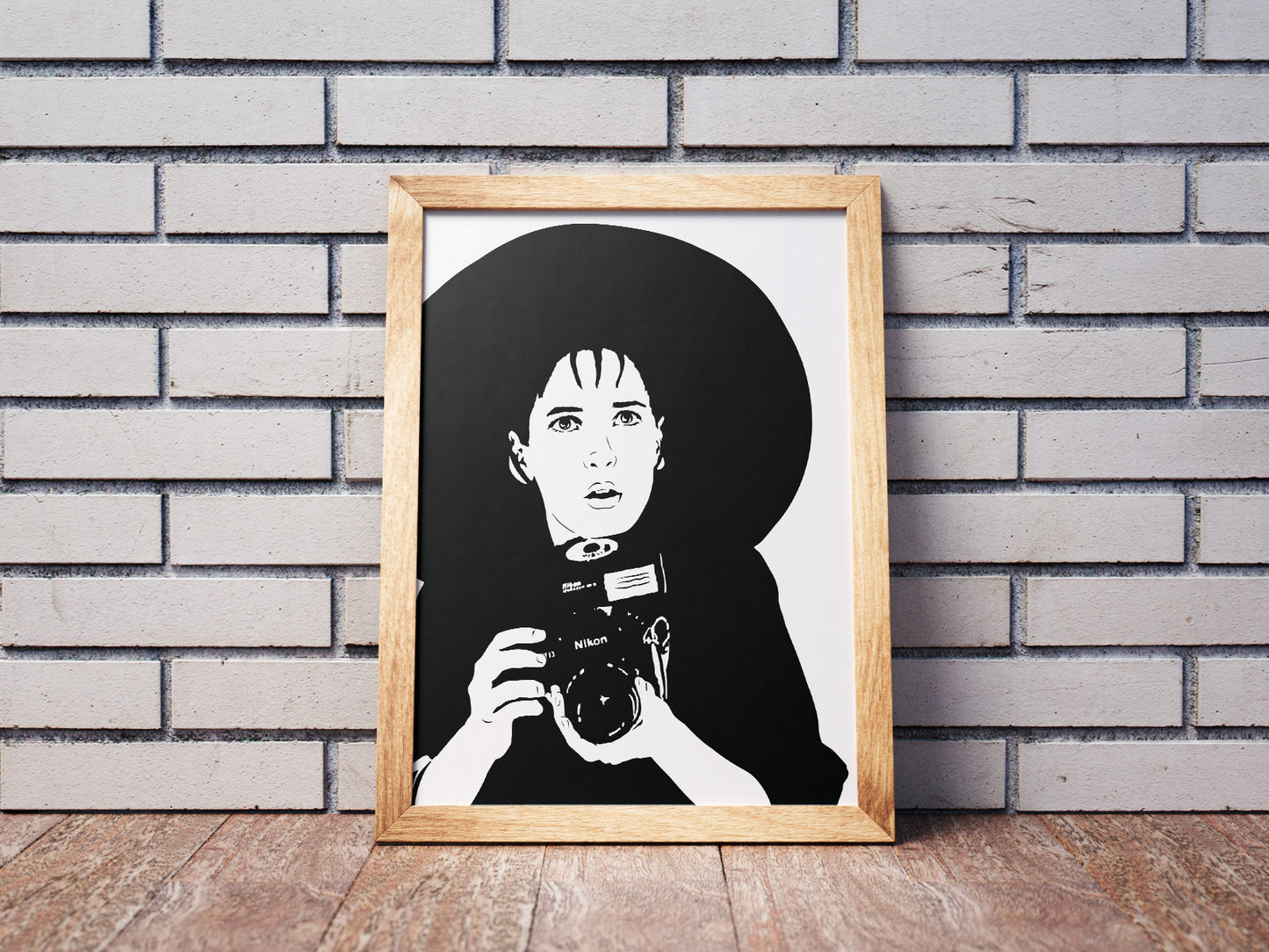 black and white illustration of lydia deetz from beetlejuice film played by winona ryder holding a nikon camera in a goth fashion outfit with a very large brimmed black hat framed art print leaned against a wall